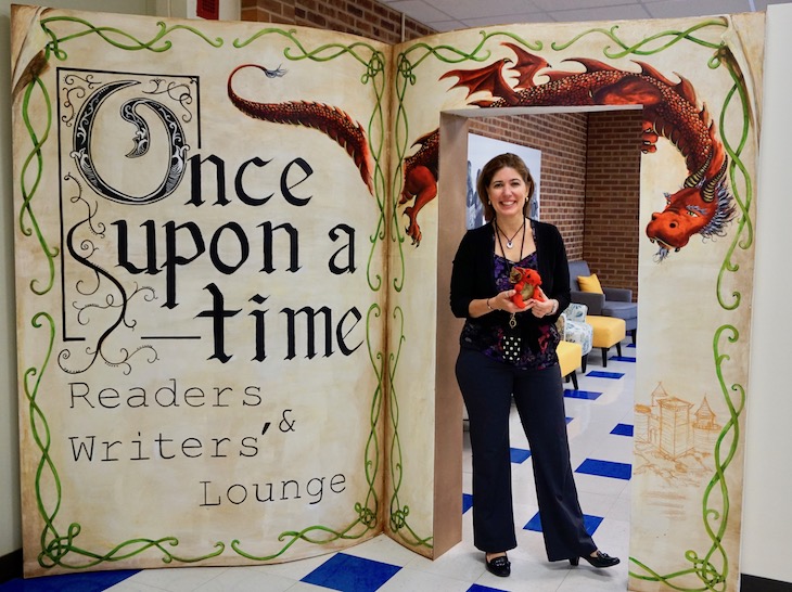 <p>H.C. Storm School Principal Anne Paonessa with the mini red dragon that sits in the bookshelf and watches over the new reading and writing space.</p>
